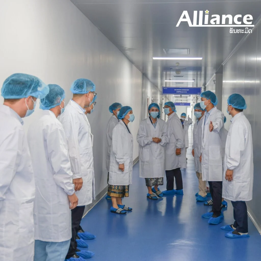Visiting ministry delegation in cleanroom gowns touring an Alliance production corridor